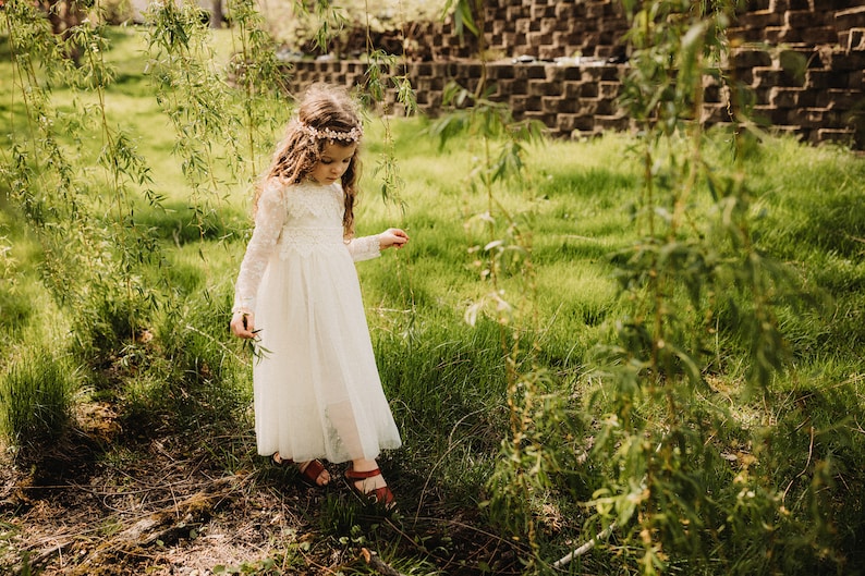 May include: A young girl wearing a white dress and a flower crown walks through a grassy field.