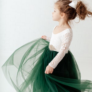 K&ouml;nnte beinhalten: Ein junges M&auml;dchen tr&auml;gt ein wei&szlig;es, lang&auml;rmliges Kleid aus Spitze mit einem gr&uuml;nen T&uuml;llrock und einem goldenen G&uuml;rtel. Sie tr&auml;gt eine wei&szlig;e Schleife im Haar.