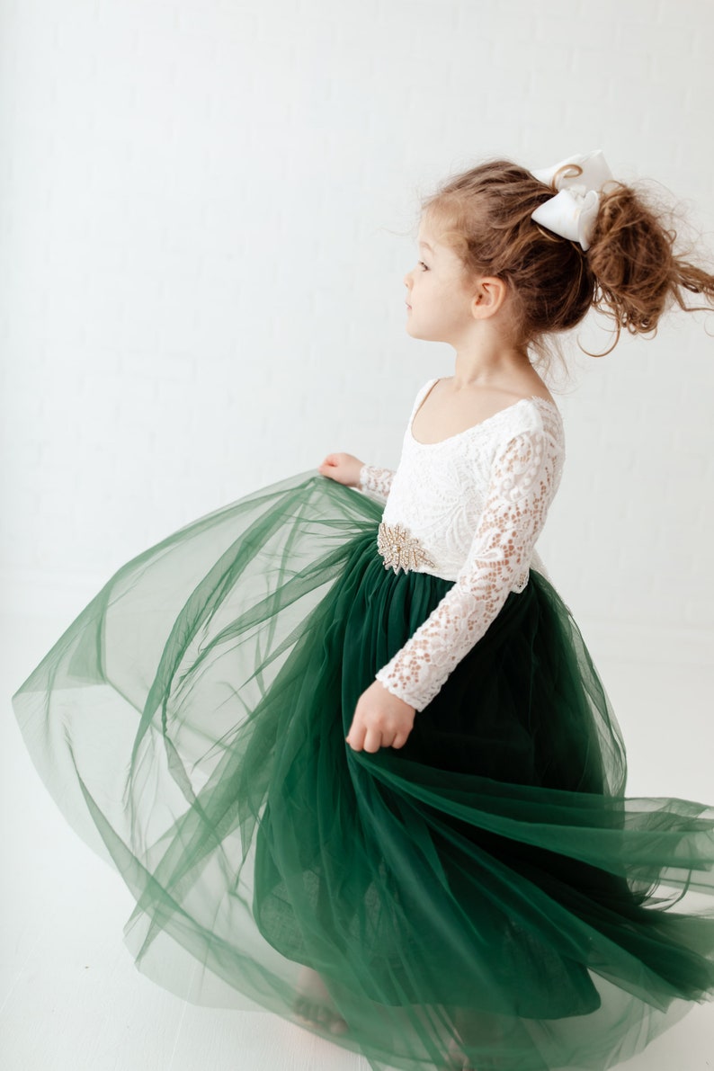 K&ouml;nnte beinhalten: Ein junges M&auml;dchen tr&auml;gt ein wei&szlig;es, lang&auml;rmliges Kleid aus Spitze mit einem gr&uuml;nen T&uuml;llrock und einem goldenen G&uuml;rtel. Sie tr&auml;gt eine wei&szlig;e Schleife im Haar.