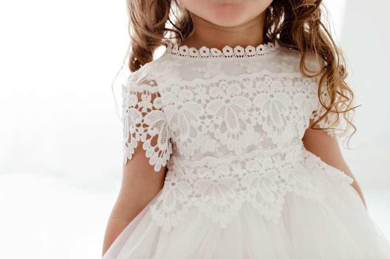 May include: A white lace dress with a high neckline and short sleeves. The dress features intricate floral lace detailing on the bodice and sleeves. The skirt appears to be made of a soft, flowing fabric. The dress is suitable for a special occasion.