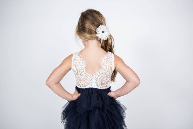 Puede incluir: Una ni&ntilde;a peque&ntilde;a con un corpi&ntilde;o de encaje blanco y una falda de tul azul marino de varias capas. El corpi&ntilde;o tiene la espalda baja y la falda est&aacute; fruncida en la cintura. La ni&ntilde;a tiene el pelo rubio con una pinza de flor blanca en el pelo.