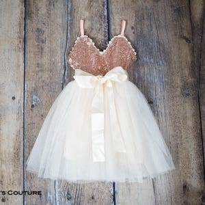 May include: A white tulle dress with a gold sequin bodice and a satin bow. The dress is ideal for a special occasion.
