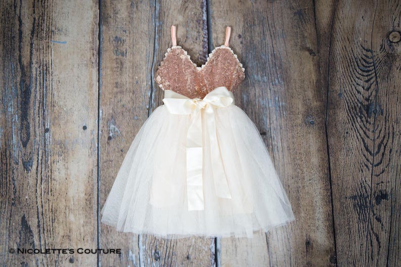 May include: A white tulle dress with a gold sequin bodice and a satin bow. The dress is ideal for a special occasion.