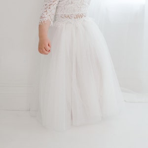 May include: A white tulle skirt with a white lace top. The skirt is full and flowing, and the top is fitted with a lace design.