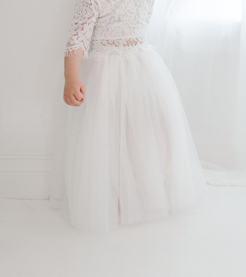 May include: A white tulle skirt with a white lace top. The skirt is full and flowing, and the top is fitted with a lace design.