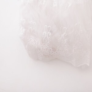 May include: White lace fabric with a delicate floral pattern. The lace is soft and sheer, and it has a romantic and elegant feel.