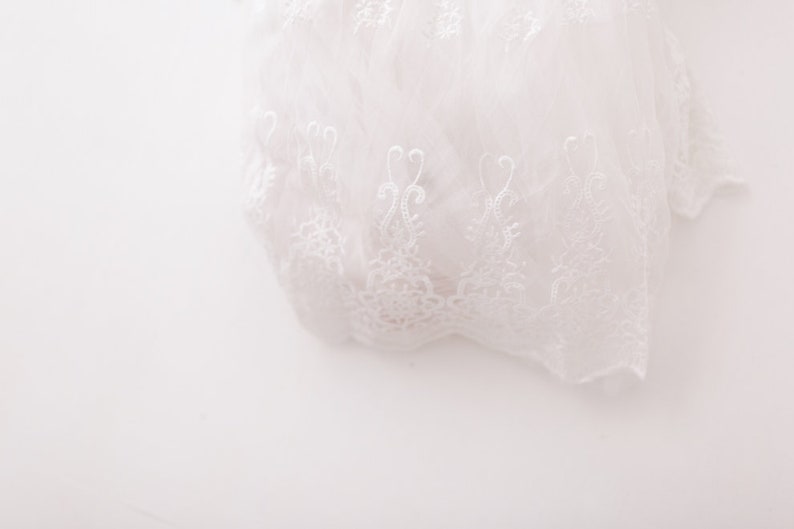 May include: White lace fabric with a delicate floral pattern. The lace is soft and sheer, and it has a romantic and elegant feel.