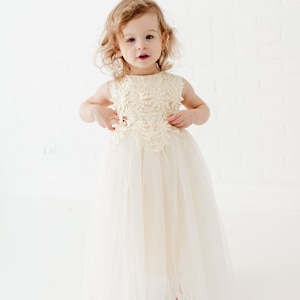 May include: A young girl wearing a white tulle dress with a floral lace bodice. The dress has a full skirt and is perfect for a special occasion.