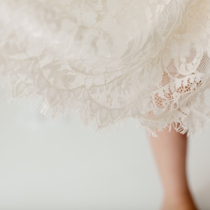 May include: A white lace skirt with a scalloped edge. The skirt is made of delicate lace and has a soft, flowing texture.