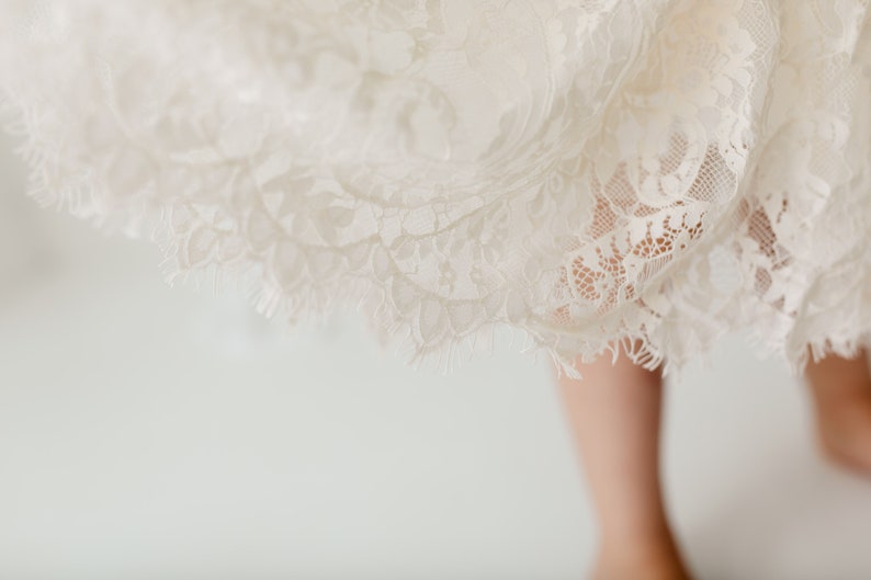 May include: A white lace skirt with a scalloped edge. The skirt is made of delicate lace and has a soft, flowing texture.