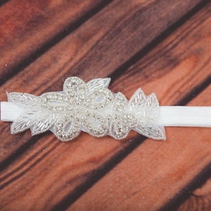 May include: A white headband with a silver beaded floral design. The headband is made of a soft, stretchy material and is perfect for adding a touch of elegance to any outfit.