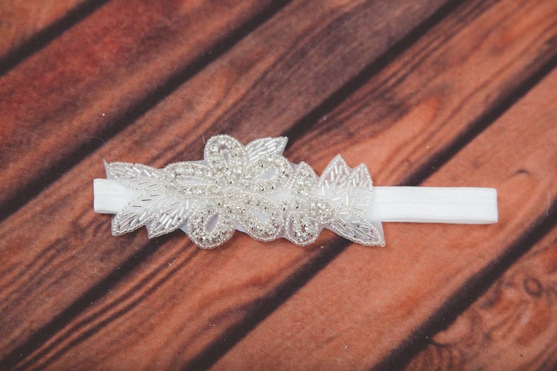 May include: A white headband with a silver beaded floral design. The headband is made of a soft, stretchy material and is perfect for adding a touch of elegance to any outfit.