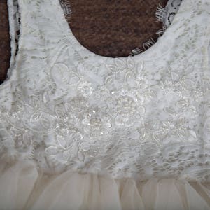 May include: A white tulle dress with a lace bodice. The bodice features a delicate floral pattern with beaded accents.