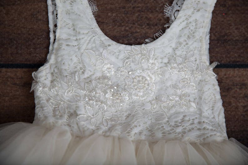 May include: A white tulle dress with a lace bodice. The bodice features a delicate floral pattern with beaded accents.