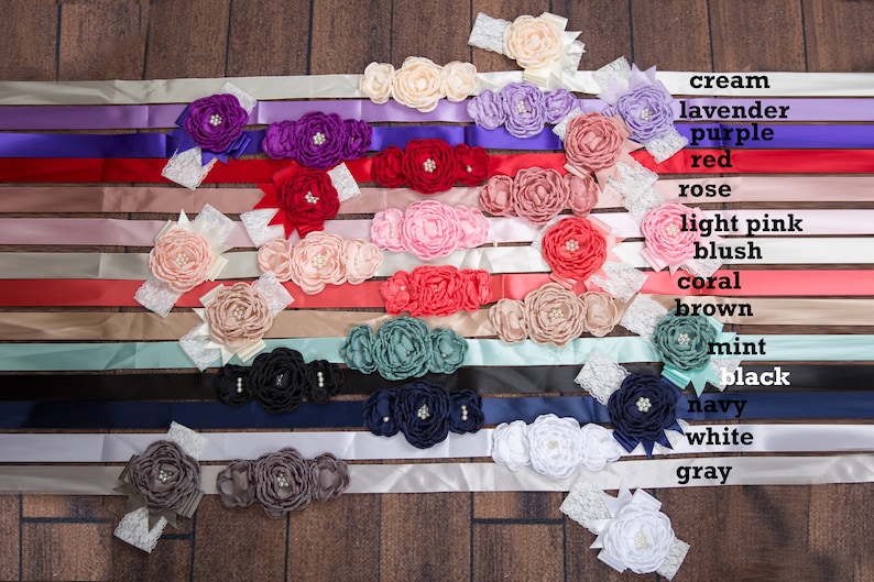 May include: A collection of 14 satin ribbon sashes with various colors and flower embellishments. The colors include cream, lavender, purple, red, rose, light pink, blush, coral, brown, mint, black, navy, white, and gray.