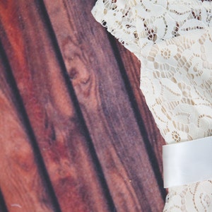 Peut inclure: Une robe en dentelle blanche avec une ceinture en satin blanc. La robe est sur un fond en bois brun.