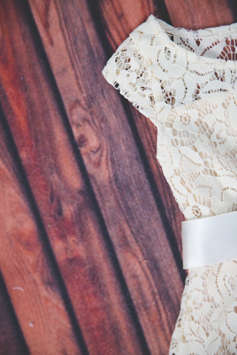 Peut inclure: Une robe en dentelle blanche avec une ceinture en satin blanc. La robe est sur un fond en bois brun.