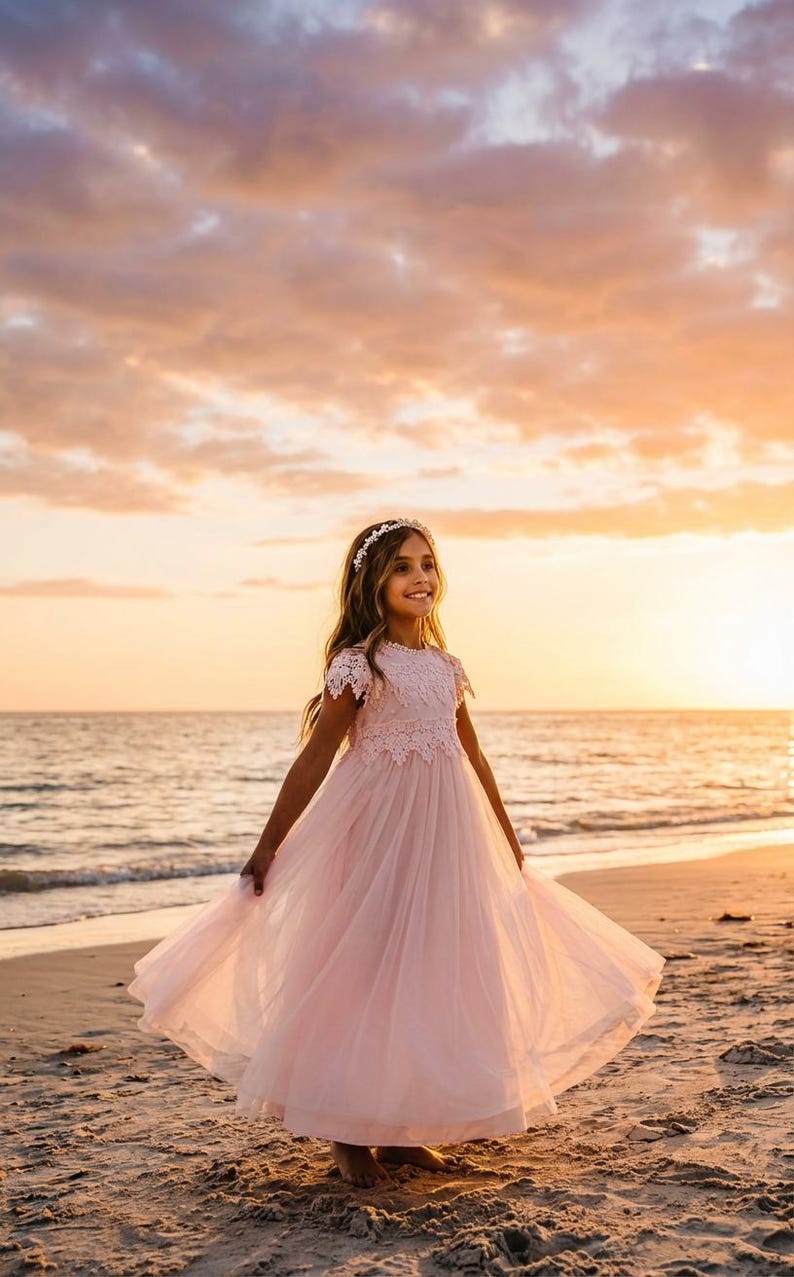 May include: A floor-length pale pink dress featuring a lace bodice with short sleeves and a full, layered tulle skirt. The garment is paired with a delicate floral headband, creating a cohesive look with a soft, flowing silhouette and intricate lace detailing.