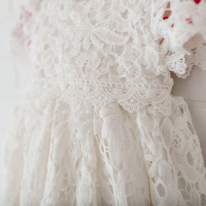 May include: White lace baby dress with a scalloped edge and short sleeves.