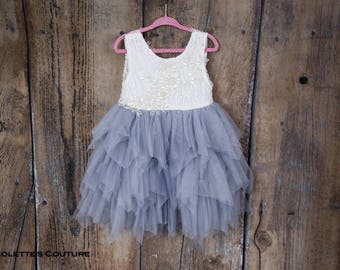 May include: A sleeveless dress featuring a white lace bodice with floral embroidery and a multi-layered, ruffled grey tulle skirt. The garment is displayed on a pink polka-dot hanger. The text NICOLETTES COUTURE is printed in the bottom left corner.