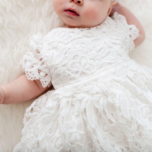 May include: A white lace baby dress with a ruffled skirt and short sleeves.