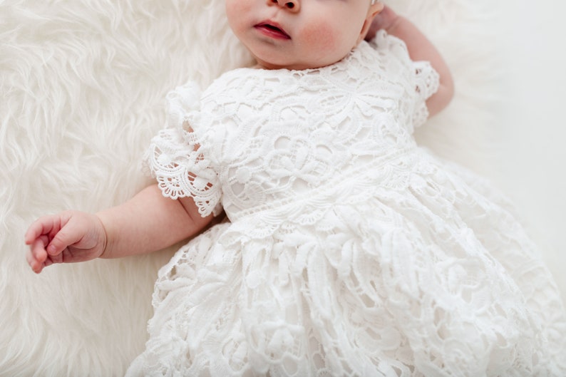 May include: A white lace baby dress with a ruffled skirt and short sleeves.