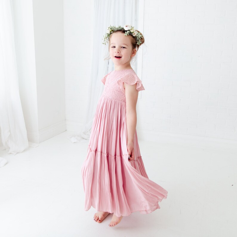 May include: A young girl wearing a pink, tiered maxi dress with a floral crown. The dress has a smocked bodice and short, ruffled sleeves.
