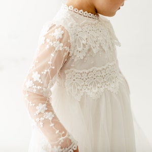 May include: A white lace dress with long sleeves and a high neckline. The dress has a delicate floral pattern and a flowing skirt.
