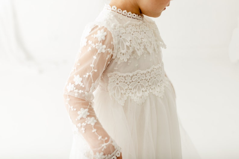 May include: A white lace dress with long sleeves and a high neckline. The dress has a delicate floral pattern and a flowing skirt.