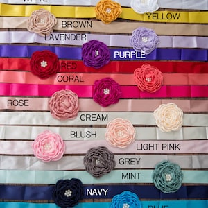 May include: A collection of satin ribbons in various colours including white, yellow, brown, lavender, purple, red, coral, rose, cream, blush, light pink, grey, mint, navy, and blue. Each ribbon features a fabric flower with a pearl centre.