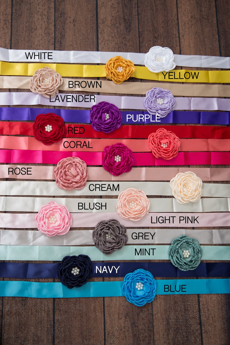 May include: A collection of satin ribbons in various colours including white, yellow, brown, lavender, purple, red, coral, rose, cream, blush, light pink, grey, mint, navy, and blue. Each ribbon features a fabric flower with a pearl centre.