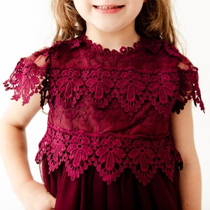 May include: A burgundy tulle dress with lace detailing. The dress has short sleeves and a round neckline. The lace is a delicate floral pattern.