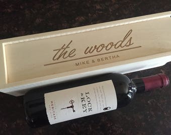 May include: A wooden box with the text "the woods" engraved on the top, along with "Mike & Bertha". The box is open and a bottle of red wine is inside. The bottle label reads "Lock & Key" and "Heritage Red Wine".
