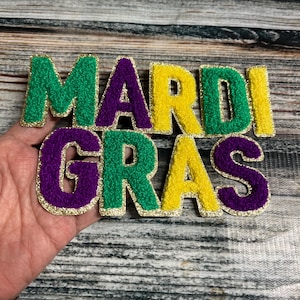 May include: Mardi Gras letters in green, yellow, and purple felt with gold glitter trim. The letters are individually cut and are approximately 3 inches tall.