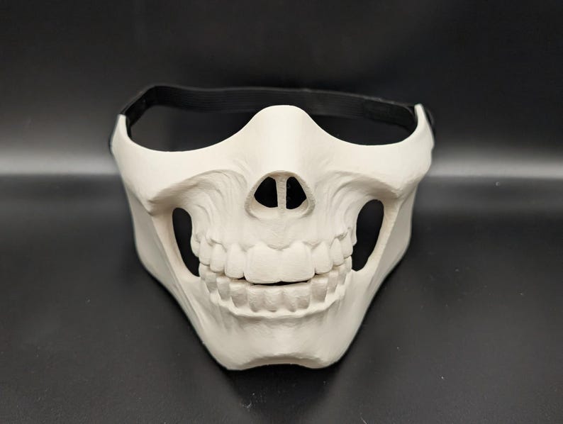White skull half mask with its black elastic strap, by Deadmoon Designs