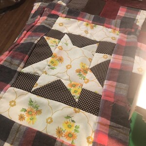 May include: A patchwork quilt with a brown, white, and pink plaid pattern. The quilt features a star design in the center, made from a white fabric with yellow floral print and brown polka dot fabric.