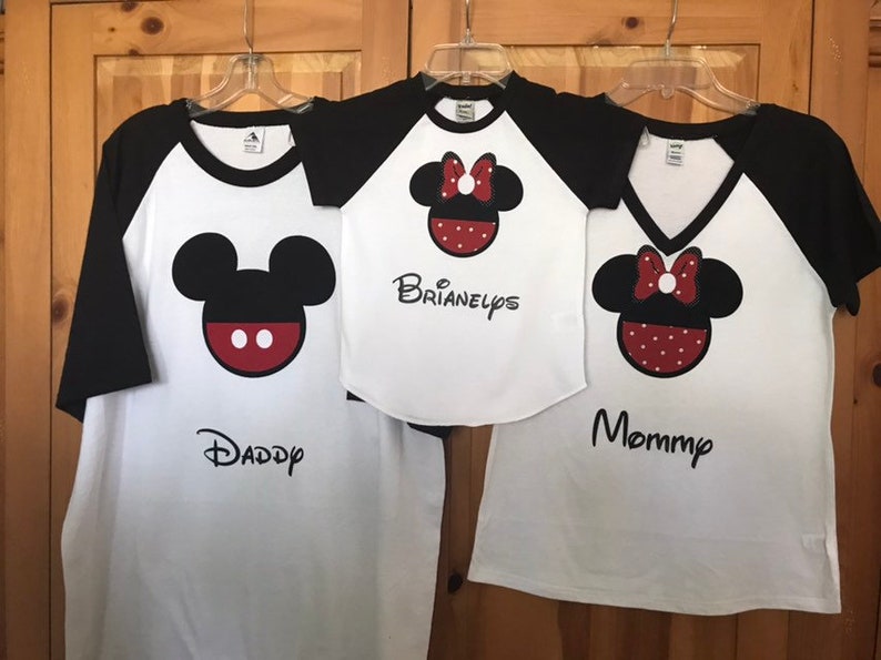 May include: Three white t-shirts with black sleeves and a Mickey Mouse or Minnie Mouse design. The shirts say "Daddy", "Mommy", and "Brianelyps".