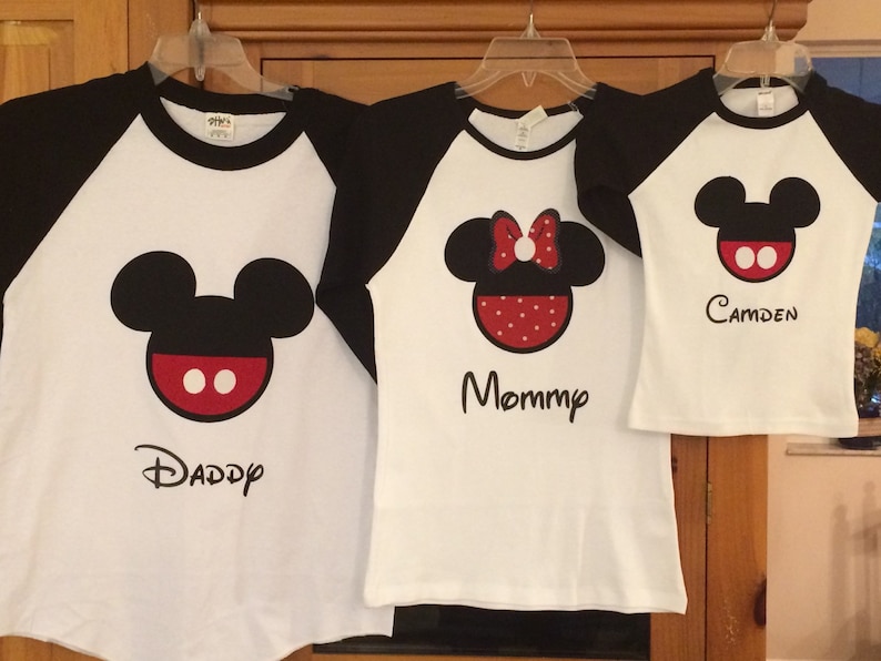 May include: Three white t-shirts with black sleeves, featuring a Mickey Mouse design and the words "Daddy", "Mommy", and "Camden".