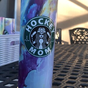 May include: A stainless steel tumbler with a marbleized purple, blue, and yellow design. The tumbler has a green and white logo that says "Hockey Mom" with a hockey stick and a woman's face wearing a hockey helmet.