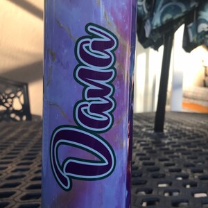May include: A purple and gold marble-patterned tumbler with the name "Dana" written in a purple and green script.