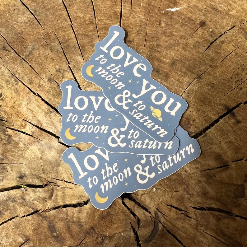 May include: Three blue stickers with the text "love you to the moon & to saturn" in white lettering. The stickers are stacked on top of each other.