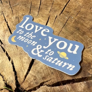 May include: A blue sticker with the text "Love you to the moon & to Saturn" in white lettering. The sticker features a crescent moon and a planet with rings in gold.