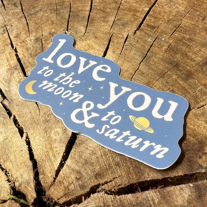 May include: A blue sticker with the text "Love you to the moon & to Saturn" in white lettering. The sticker features a crescent moon and a planet with rings in gold.