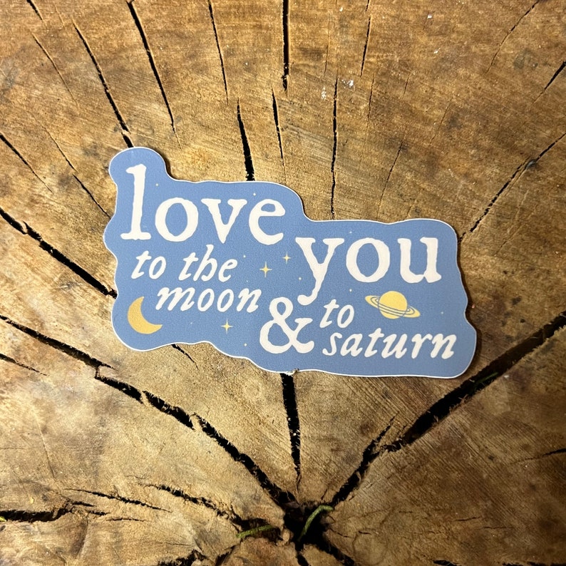 May include: A blue sticker with white text that reads "love you to the moon & to saturn". The sticker features a crescent moon and a planet with rings.