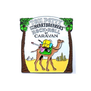 May include: A colorful pin featuring a camel carrying luggage, a guitar, and the text "TOM PETTY AND THE HEARTBREAKERS ROCK'N'ROLL '87 CARAVAN". The pin has a desert theme with palm trees and pyramids.