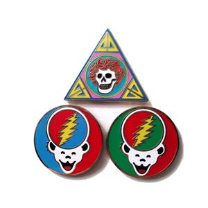 May include: Three enamel pins featuring iconic imagery. One is a blue, yellow, and pink triangle with a skull and roses. The other two are round, with a lightning bolt and a smiling bear face, one in red and blue, the other in red and green.