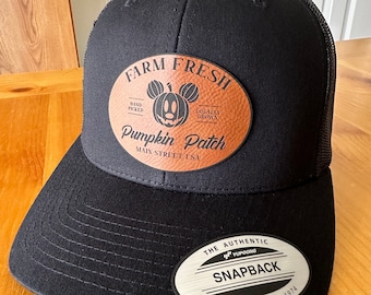 May include: Black and brown baseball cap with a leather patch that says "Farm Fresh Pumpkin Patch Main Street USA" and a Mickey Mouse head with a pumpkin face. The patch has a brown leather background and white stitching. The cap has a black mesh back and a black snap closure with a silver label that says "The Authentic YUPOONG Snapback YUPOONG Since 1974".