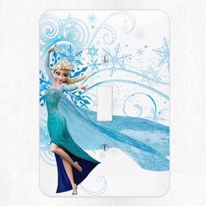 May include: A light switch cover featuring a cartoon image of Elsa from the movie Frozen. Elsa is wearing a blue and green dress and is surrounded by snowflakes and swirls.