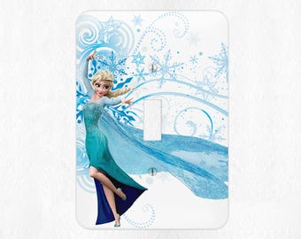 Op de afbeelding: Een lichtschakelaar-afdekplaat met een cartoonafbeelding van Elsa uit de film Frozen. Elsa draagt een blauwe en groene jurk en is omringd door sneeuwvlokken en swirls.