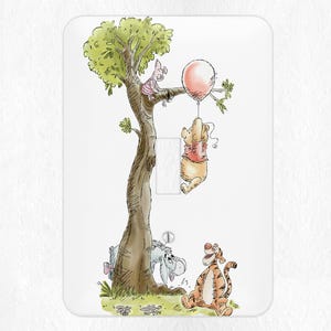 May include: A Winnie the Pooh light switch cover featuring Winnie the Pooh, Piglet, and Tigger. The characters are drawn in a cartoon style and are surrounded by a green tree and a pink balloon.